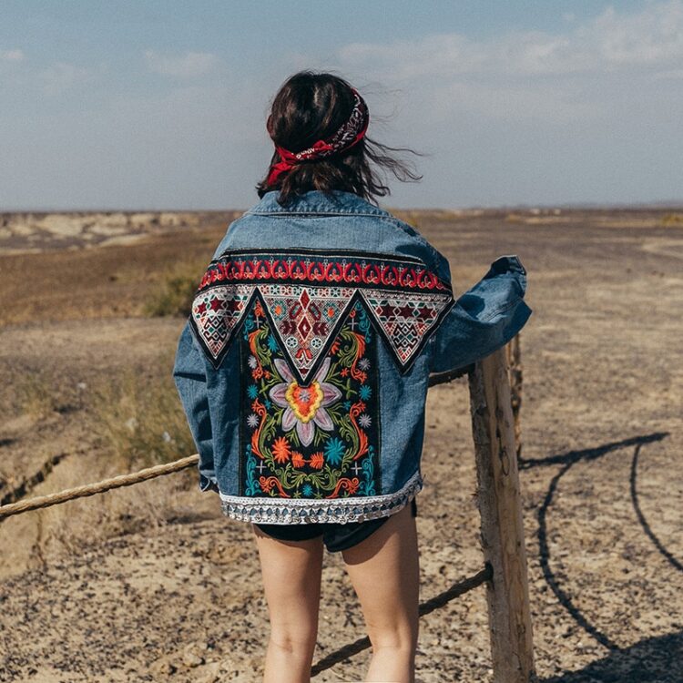 Veste en jean brodée style bohème à fleurs porté par une femme au bandana rouge devant un desert