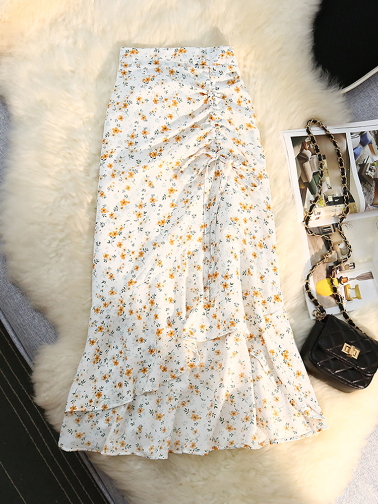 Jupe blanche avec des fleurs jaunes étalée sur un tapis en fausse fourrure avec un sac à bandoulière noir à gauche ainsi qu'un magazine.
